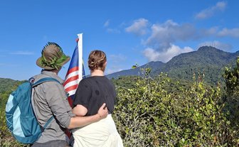 Teenager mit malaysischer Flagge und For Family Reisen Rucksack genießen den Ausblick nach der Coral Hill-Wanderung in den Cameron Highlands - Malaysia Familienreise