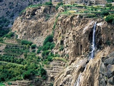 Aussicht auf die Felslandschaft des Jebel Akhdar mit einem kleinen Wasserfall inmitten der grünen Täler – Oman Reise mit Kindern