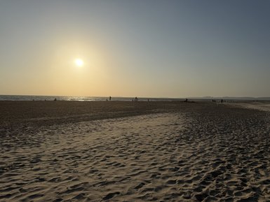 Ein ruhiger Strand bei Sonnenuntergang, mit sanften Wellen und Menschen, die am Wasser spazieren gehen.