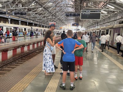 Eine Gruppe von Kindern steht am Bahnhof Chhatrapati Shivaji Maharaj und beobachtet die vorbeifahrenden Züge.