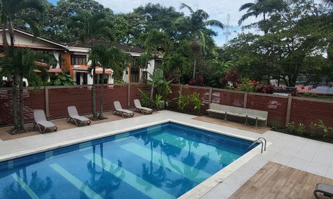 Ein einladender Poolbereich mit blauen Wasser und Liegen, umgeben von üppigem Grün und einem klaren Himmel.