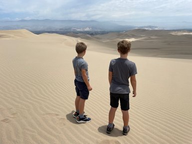 Zwei Jungen stehen am Rand einer Sanddüne und blicken auf die weite, trockene Landschaft der Huacachina-Oase.