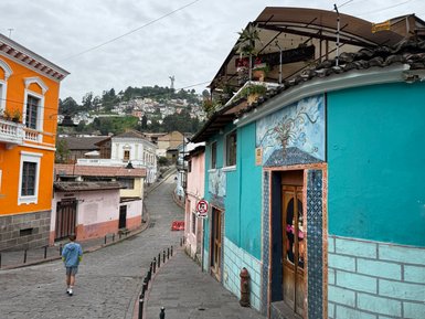 Eine schmale, gepflasterte Straße führt an bunten Häusern vorbei, während ein Junge in blauer Jacke spaziert.
