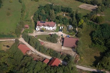 Eine Luftaufnahme zeigt ein weitläufiges Gelände mit einem großen, weißen Gebäude und mehreren roten Dächern in der Umgebung.