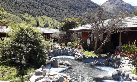Eine malerische Landschaft mit einem klaren Wasserlauf, umgeben von üppigem Grün und rustikalen Holzhütten.