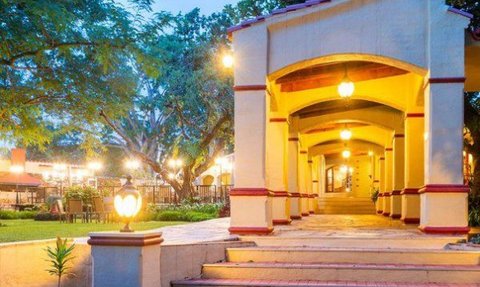 Ein einladender, beleuchteter Gang mit Bögen führt durch eine grüne Landschaft, umgeben von Bäumen und Pflanzen.