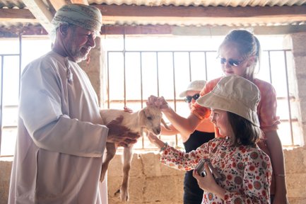 Kinder begegnen einer Ziege bei einem Zwischenstopp auf einer Farm zwischen Canyon und Wüste – Oman Familienreise