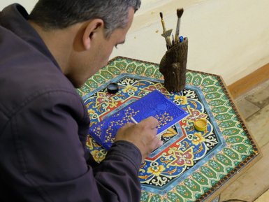 Ein Künstler konzentriert sich auf die Miniaturmalerei, während er feine Details auf einer blauen Fläche hinzufügt.