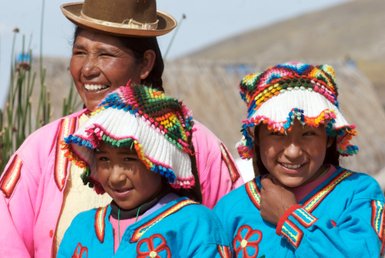 Eine fröhliche Uros-Familie posiert in traditioneller Kleidung auf den schwimmenden Inseln des Titicacasees.