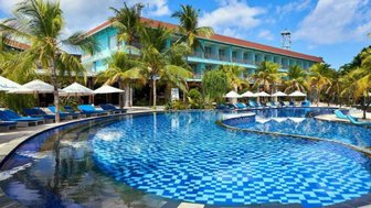 Ein luxuriöser Pool mit blauen Fliesen, umgeben von Palmen und Liegen, unter einem strahlend blauen Himmel.
