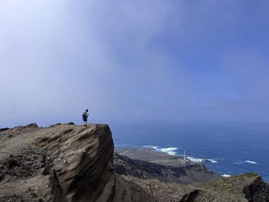 Ein Junge steht auf einer Klippe und blickt auf das weite Meer, während ein Leuchtturm in der Ferne sichtbar ist.