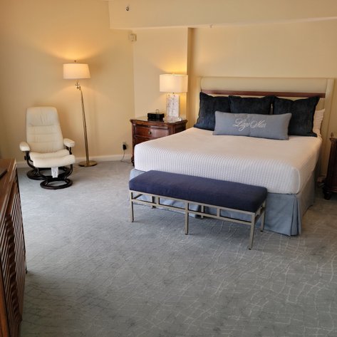 Ein elegantes Hotelzimmer mit einem großen Bett, das mit blauen Kissen dekoriert ist, und einem gemütlichen Sessel in der Ecke.