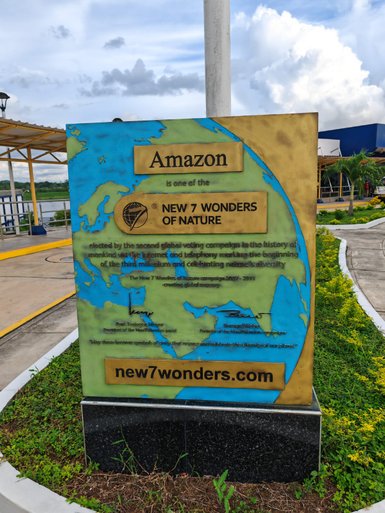 Ein Schild, das den Amazonas als eines der neuen sieben Naturwunder der Welt auszeichnet, umgeben von grüner Landschaft.