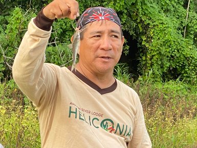 Ein Mann hält stolz einen gefangenen Fisch in der Hand, umgeben von üppigem, grünem Dschungel im Amazonasgebiet.