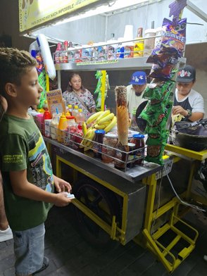 Ein Junge steht an einem Straßenstand, der mit bunten Snacks, Getränken und frischen Früchten gefüllt ist.