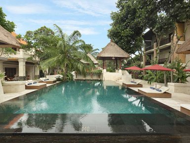 Ein ruhiger Poolbereich in Bali, umgeben von tropischen Pflanzen und Sonnenliegen unter roten Sonnenschirmen.