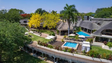 Eine weitläufige Hotelanlage mit einem Pool, umgeben von üppigem Grün und bunten Blumen, strahlt tropisches Flair aus.
