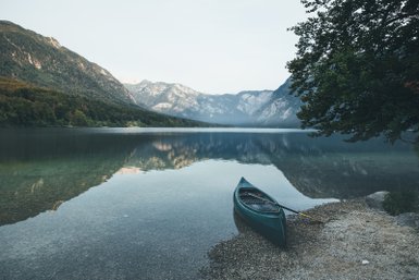 Ein ruhiger See umgeben von majestätischen Bergen, mit einem Kanu, das sanft am Ufer liegt und die Landschaft spiegelt.
