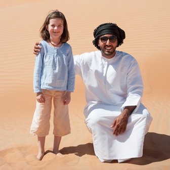Mädchen steht neben einem Beduinen in der Wüste Omans – Oman mit Kindern