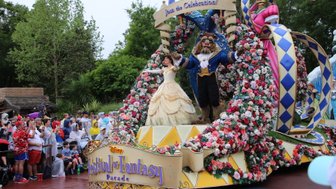 Eine festliche Parade im Magic Kingdom zeigt Belle und das Biest, umgeben von bunten Blumen und fröhlichen Zuschauern.