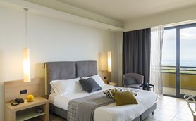 Ein modernes Hotelzimmer mit einem großen Bett, eleganten Lampen und einem Balkon mit Meerblick.