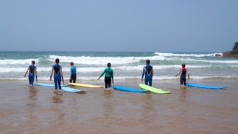 Sechs Surfer stehen im flachen Wasser des Strandes, bereit, die Wellen des Algarve zu erobern.