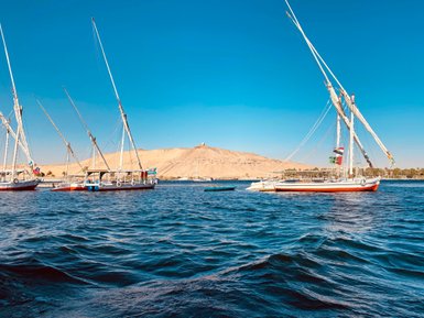 Zwei traditionelle Segelboote schaukeln sanft auf dem blauen Wasser, während der klare Himmel über der Wüstenlandschaft strahlt.