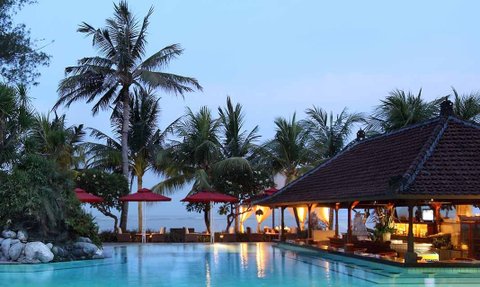 Ein ruhiger Poolbereich in Bali, umgeben von Palmen und einem traditionellen balinesischen Pavillon im Abendlicht.