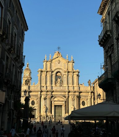 Eine belebte Straße führt zu einer beeindruckenden Kirche mit goldenen Verzierungen und einem strahlend blauen Himmel.