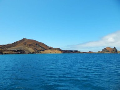 Eine atemberaubende Küstenlandschaft mit sanften Hügeln und klarem, blauem Wasser unter einem strahlend blauen Himmel.