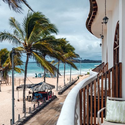 Eine Aussicht von einem Balkon auf einen Strand mit Palmen und einem kleinen Strandpavillon, der im Sand steht.