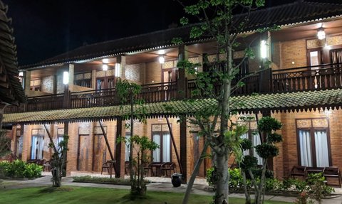 Ein charmantes Hotelgebäude mit Holzverkleidung und Balkon, umgeben von gepflegtem Grün und sanfter Beleuchtung in der Nacht.