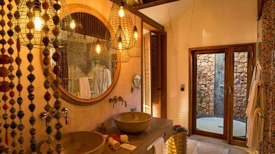 Ein stilvolles Badezimmer mit zwei runden Waschbecken, umgeben von warmem Licht und einem rustikalen Steinwand-Duschbereich.
