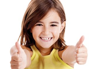 Ein fröhliches Mädchen mit braunen Haaren lächelt breit und zeigt beiden Daumen nach oben.