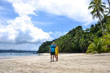 Ein Paar steht gemeinsam am Strand von Isla Coiba, umgeben von tropischen Palmen und einer malerischen Küstenlandschaft.