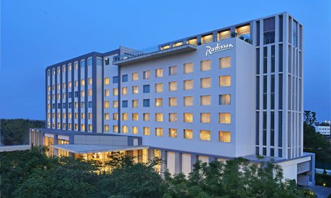 Das Radisson Hotel in Agra strahlt in der Dämmerung mit beleuchteten Fenstern und modernem Design, umgeben von Bäumen.