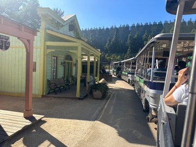 Eine belebte Straße in einem Themenpark, mit bunten Gebäuden und einem Zug voller Passagiere, die die Umgebung genießen.
