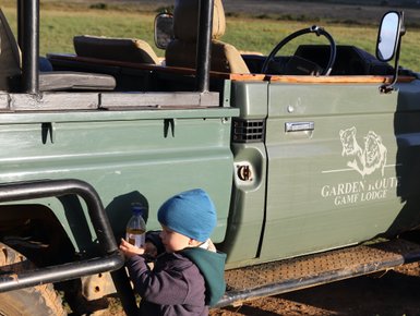 Kleines Kind steht neugierig neben einem Safari-Jeep in der Garden Route Game Lodge – Garden Route Reise mit Kindern