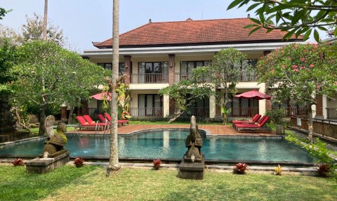 Ein ruhiger Hotelgarten mit einem Pool, umgeben von üppigem Grün und roten Liegen unter Sonnenschirmen.