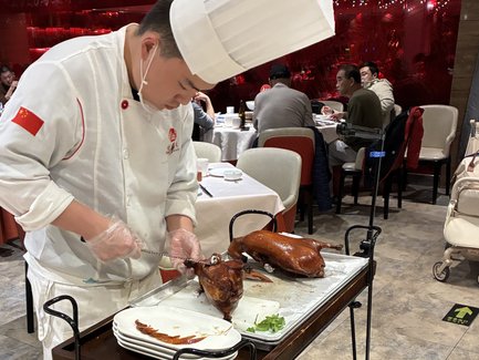 Ein Koch in einem Restaurant schneidet sorgfältig eine knusprige Pekingente auf einem Servierwagen für die Gäste.