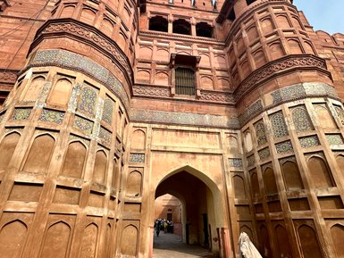 Ein historisches rotes Fort mit beeindruckender Architektur und einer Person, die in traditioneller Kleidung durch den Eingang geht.