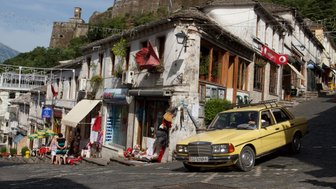 Eine gelbe Limousine parkt an einer steilen, gepflasterten Straße, umgeben von historischen Gebäuden und Geschäften.