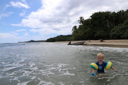 Kleines Kind planscht fröhlich im seichten Wasser am Strand – Costa Rica Reise mit Kindern