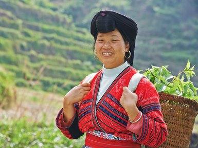 Einheimische Frau der Yao-Minderheit mit traditioneller Kleidung lächelt in die Kamera vor den Reisterrassen von Longsheng – China Familienreise