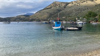 Ein ruhiger Hafen mit mehreren Booten, umgeben von sanften Hügeln und klarem Wasser, das die Landschaft widerspiegelt.