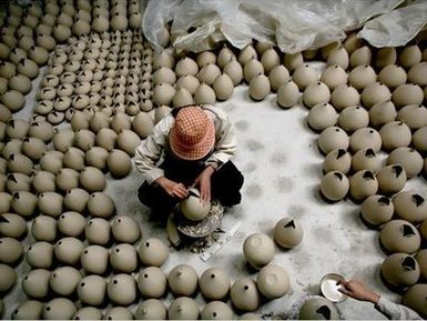 Ein Töpfer arbeitet konzentriert an einem Keramikstück, umgeben von zahlreichen unglasierten Töpfen in einer Werkstatt.