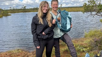 Zwei Frauen stehen am Ufer eines Gewässers, beide tragen Schneeschuhe und lächeln in die Kamera.