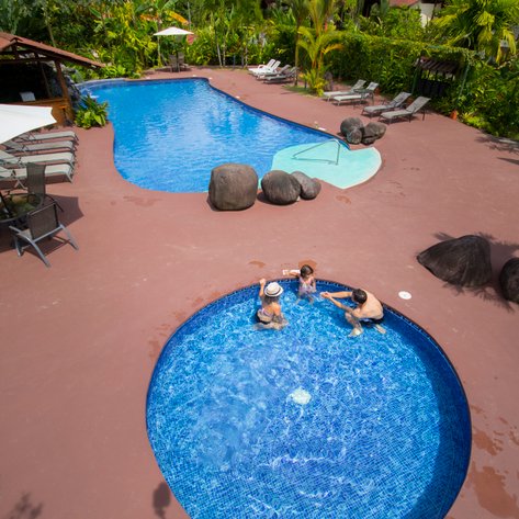 Ein entspannender Poolbereich mit zwei Schwimmbecken, umgeben von üppigem Grün und Sonnenliegen für Gäste.