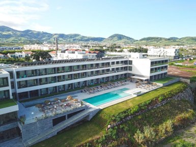 Ein modernes Hotel mit einem großen Pool und Liegen, umgeben von grünen Hügeln und einer malerischen Landschaft.