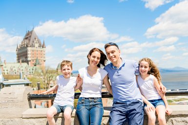 Eine glückliche Familie posiert vor dem beeindruckenden Château Frontenac, umgeben von strahlend blauem Himmel und Wolken.